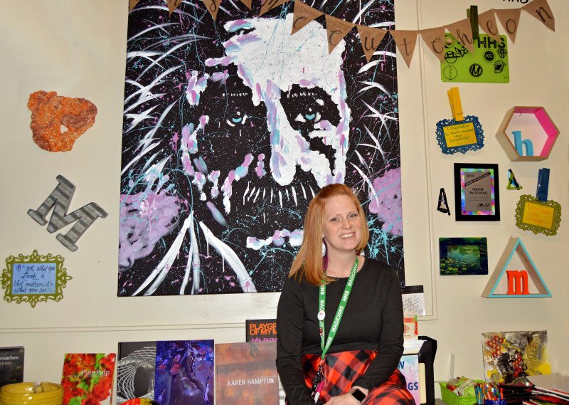 Heather McCutcheon sits in her classroom in front of a wall of artwork.