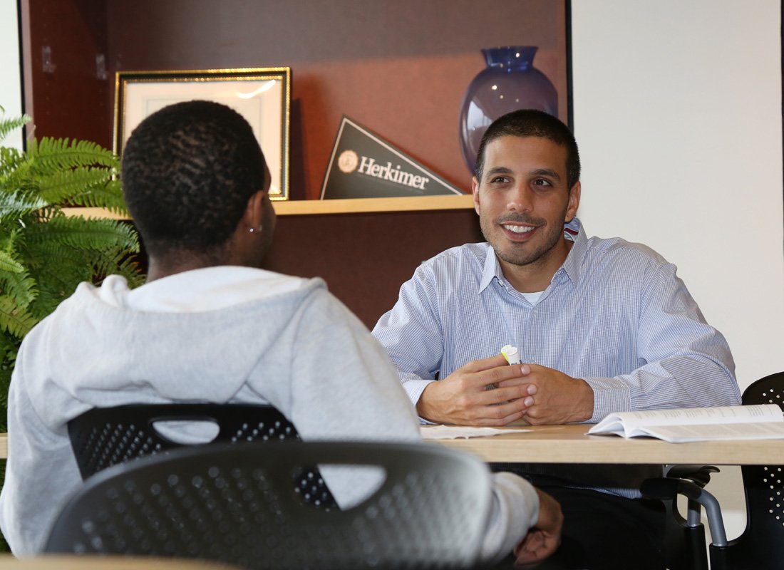 Advisor meeting with a student at a desk, discussing coursework in an office setting. Identified as informative because it shows a student support interaction relevant to academic advising.